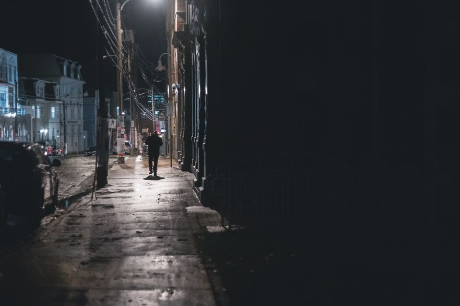 Person seen from behind walks down a historic New Orleans street at dusk, observing the surroundings with cast iron balcon...